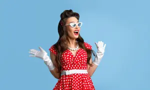 Kobieta w czerwonej sukience w grochy, białych rękawiczkach i okularach w stylu pin up girl stylizacje, z uniesionymi rękami.