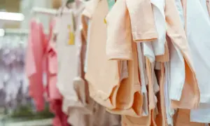 Ubranka dla niemowląt wiszą na wieszakach. Różowe, brzoskwiniowe i białe body, idealne na roczne dziecko rozmiar.