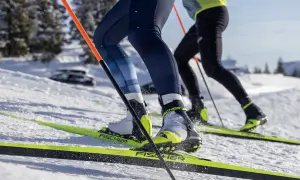 Zbliżenie na buty narciarskie i narty biegowe dwóch osób na ośnieżonym stoku.