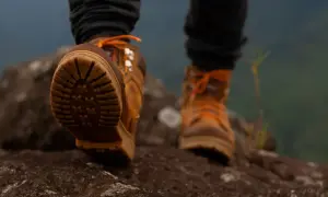 Wysokie buty trekkingowe z pomarańczowymi sznurówkami i wodoodporną membraną w butach, stawiające pierwsze kroki na skalistym szlaku.