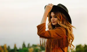 Kobieta w kapeluszu i kurtce z frędzlami, styl boho.