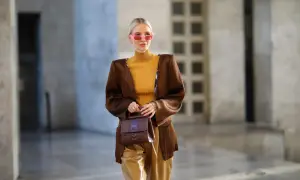 Elegancka brązowa torebka dopełnia stylizację z musztardowym golfem i błyszczącymi spodniami.
