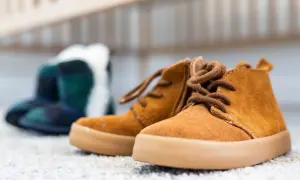 Brązowe, sznurowane buty dziecięce na pierwszym planie, w tle niebiesko-zielone kalosze.