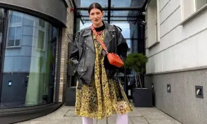 Kobieta w skórzanej ramonesce i żółtej sukience w kwiaty, z pomarańczową torebką na ramieniu.