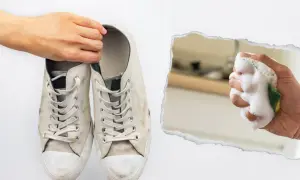 Brudne białe trampki trzymane przez rękę, obok spieniona gąbka do czyszczenia.