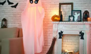 Duch z czarnymi oczami, dynia, kominek i nietoperze na ścianie - dekoracje na Halloween.