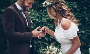 Para wesele w stylu boho: pan młody w brązowej marynarce i muszce, panna młoda w białej sukience i wianku.
