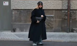 Elegancka stylizacja płaszcz i adidasy. Kobieta w czarnym płaszczu, jeansach i czapce z daszkiem, trzyma torebkę.