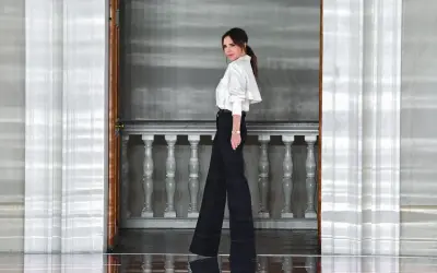 Victoria Beckham w eleganckim, białym topie i szerokich czarnych spodniach, uosobienie stylu.