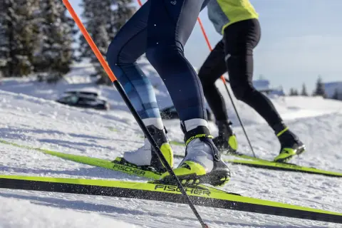 Zbliżenie na buty narciarskie i narty biegowe dwóch osób na ośnieżonym stoku.