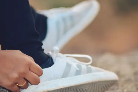 Dłoń z pierścionkiem dotyka białego buta Adidas. Idealna rozmiarówka Adidasa zapewnia komfort.