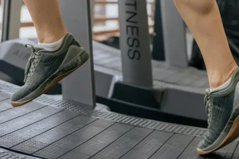 Dobre buty na bieżnię to klucz do komfortowego treningu. Na zdjęciu widać nogi w zielonych, sportowych butach na bieżni.