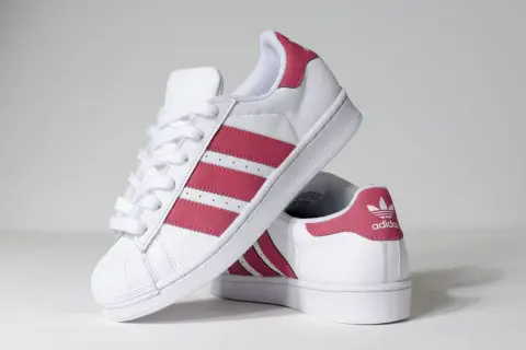 Białe buty Adidas Superstar z różowymi paskami i logo.