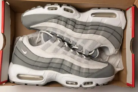 Szare i białe buty sportowe Nike Air Max 95, znane jako ermaksy, leżą w kartonowym pudełku.