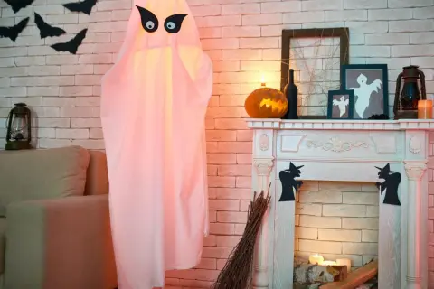 Duch z czarnymi oczami, dynia, kominek i nietoperze na ścianie - dekoracje na Halloween.
