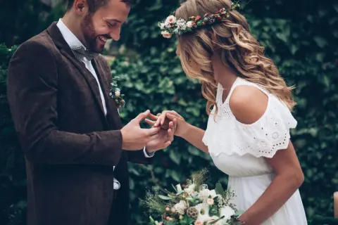 Para wesele w stylu boho: pan młody w brązowej marynarce i muszce, panna młoda w białej sukience i wianku.
