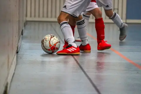 Piłka nożna na hali, gracze w czerwonych butach i białych strojach. Czy w turfach można grać na hali? Tak, to właśnie dzieje się na tym zdjęciu!