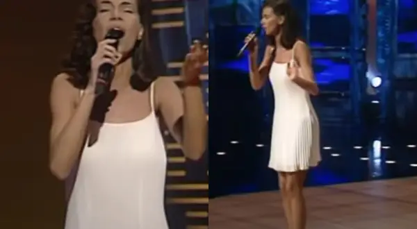 Edyta Górniak w białej sukience na scenie, śpiewa do mikrofonu.