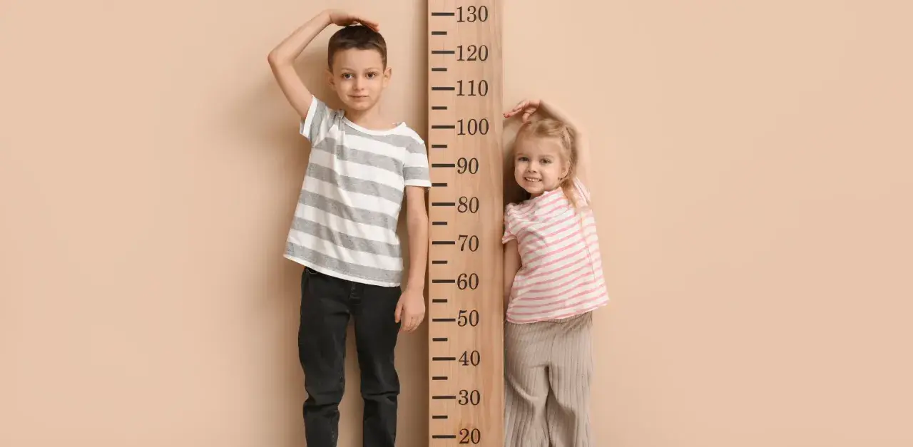 Chłopiec i dziewczynka mierzą wzrost przy drewnianej miarce. Chłopiec ma ok. 115 cm, dziewczynka ok. 85 cm. Rozmiar 68 jaki wiek?