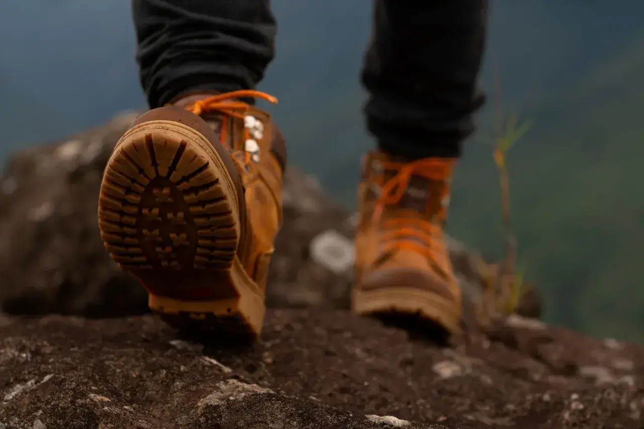 Wysokie buty trekkingowe z pomarańczowymi sznurówkami i wodoodporną membraną w butach, stawiające pierwsze kroki na skalistym szlaku.