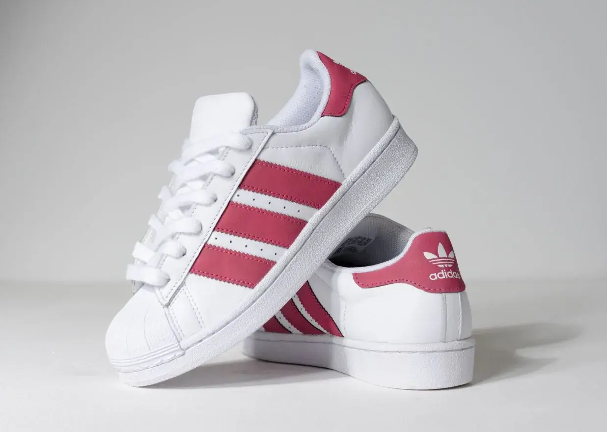 Białe buty Adidas Superstar z różowymi paskami i logo.