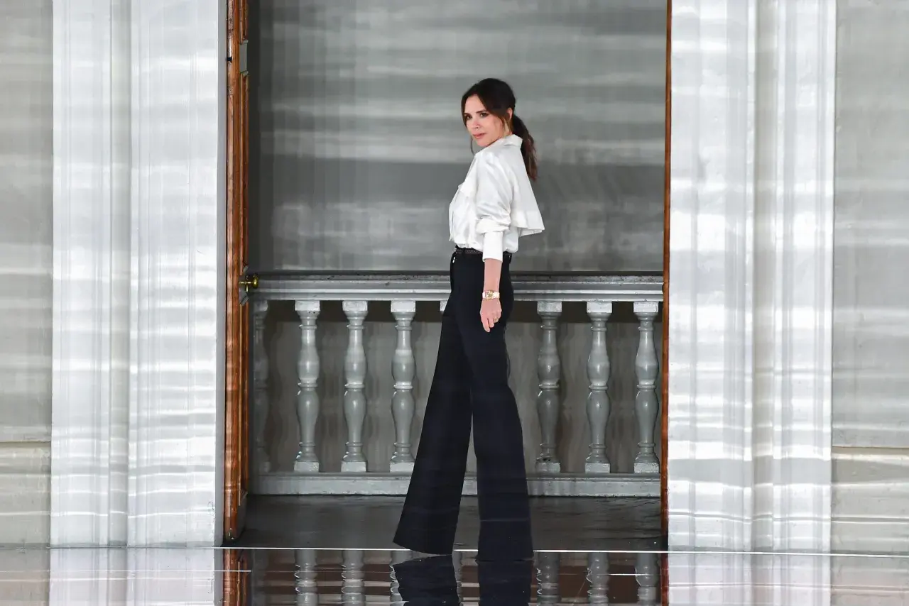 Victoria Beckham w eleganckim, białym topie i szerokich czarnych spodniach, uosobienie stylu.