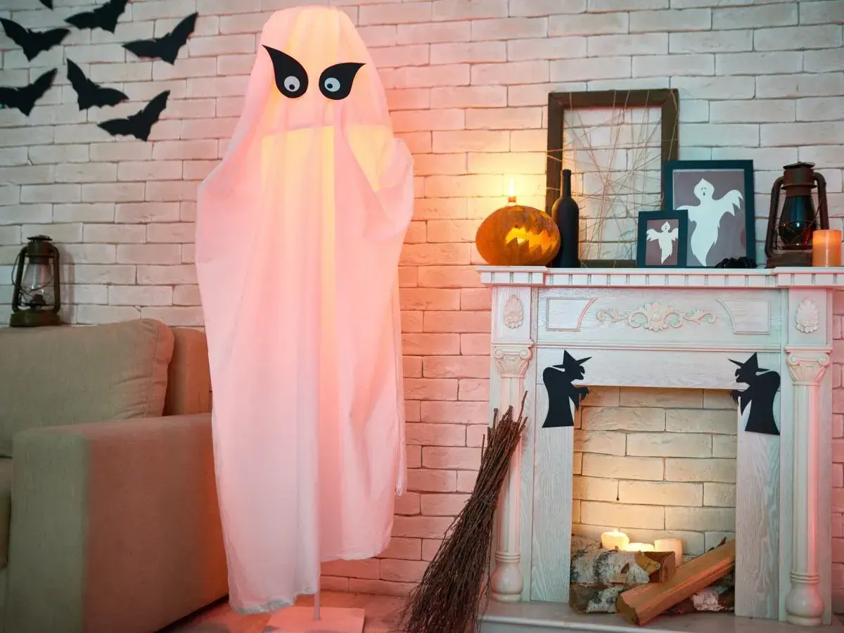 Duch z czarnymi oczami, dynia, kominek i nietoperze na ścianie - dekoracje na Halloween.