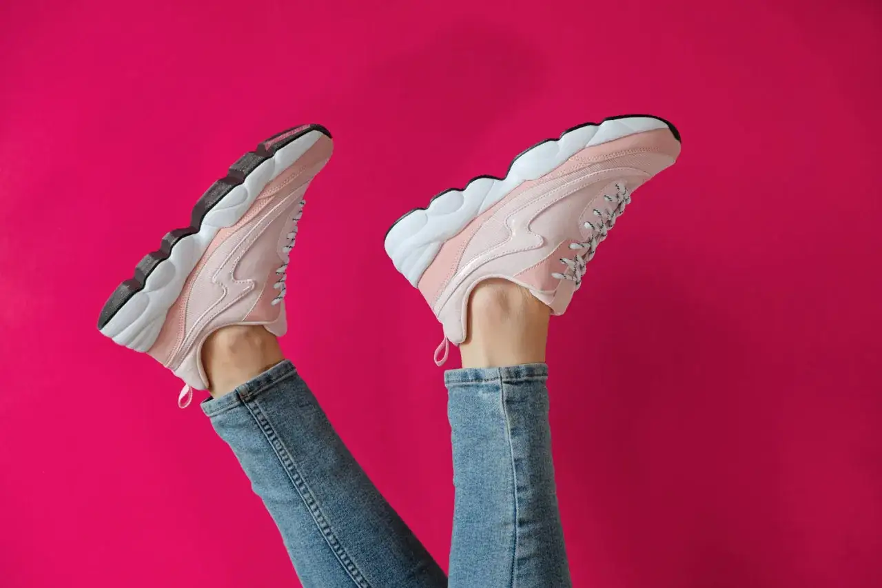 Nogi w dżinsach i amarantowych sneakersach na fuksjowym tle.
