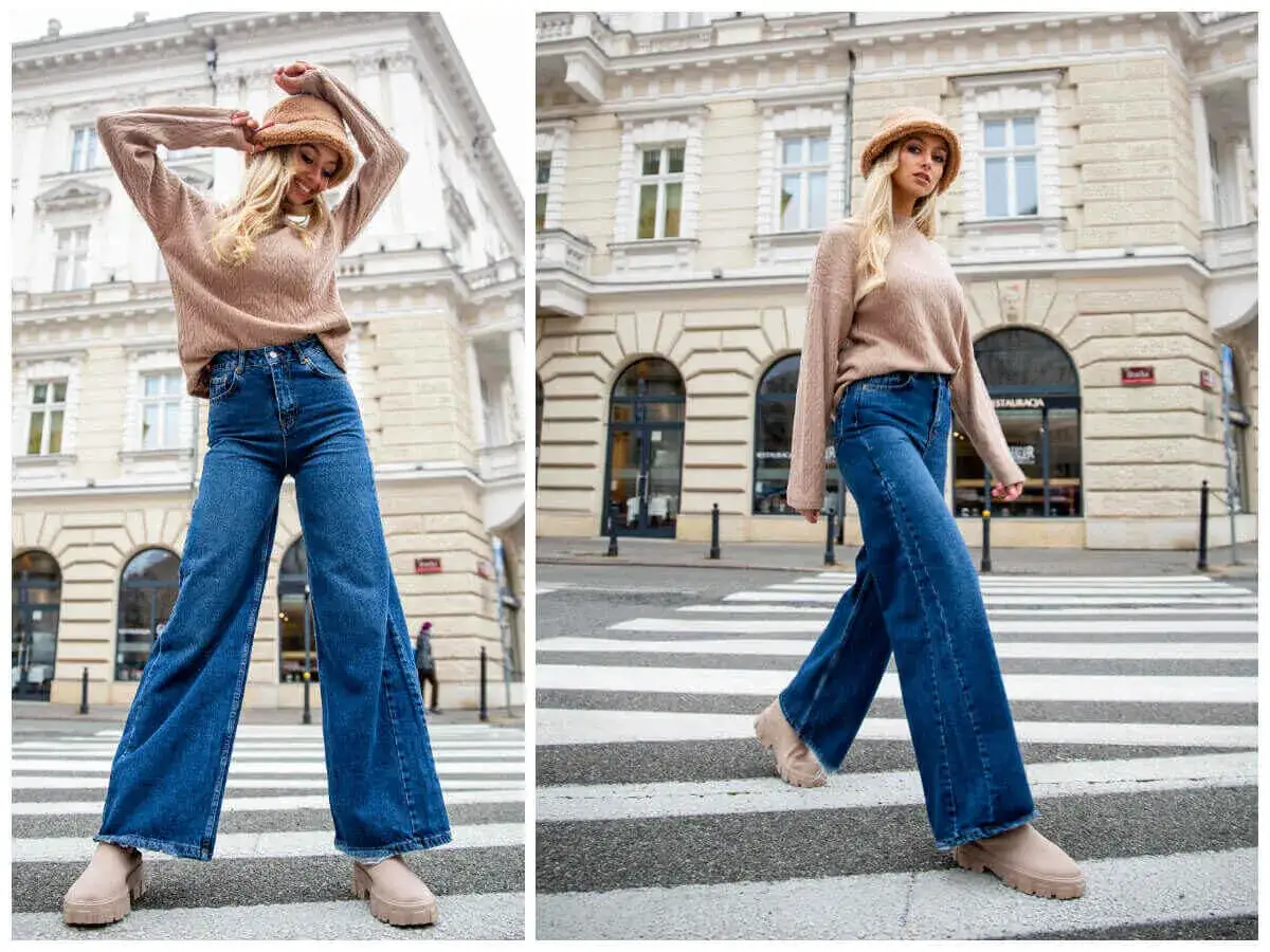 Modna kobieta w szerokich jeansach i beżowym swetrze, prezentująca stylizacje na tle miejskiej kamienicy.