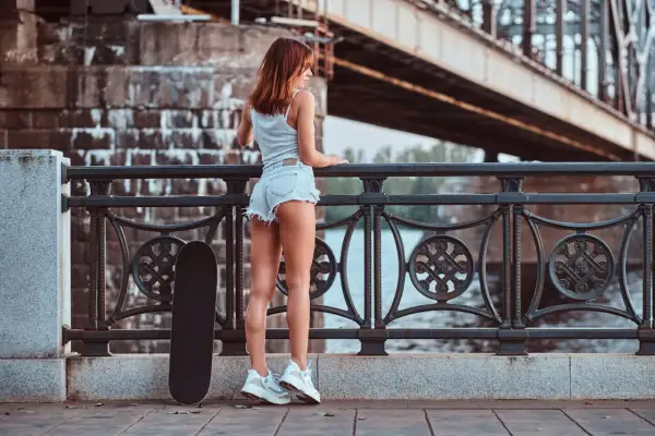 Dziewczyna w krótkich spodenkach i białych sneakersach, obok deskorolka. Idealne buty do krótkich spodenek damskich na miejskie wypady.