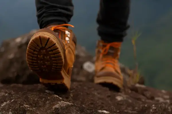 Wysokie buty trekkingowe z pomarańczowymi sznurówkami i wodoodporną membraną w butach, stawiające pierwsze kroki na skalistym szlaku.