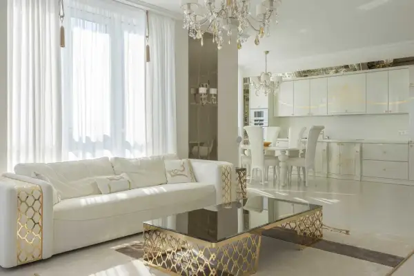 Elegancki salon i kuchnia w stylu glamour, z białymi meblami, złotymi zdobieniami i kryształowym żyrandolem.