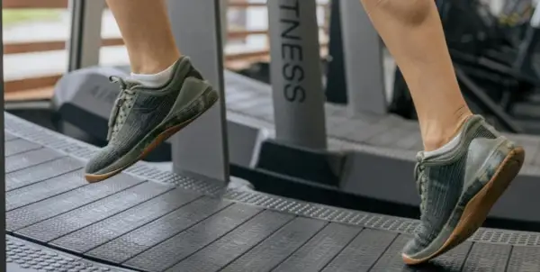 Dobre buty na bieżnię to klucz do komfortowego treningu. Na zdjęciu widać nogi w zielonych, sportowych butach na bieżni.