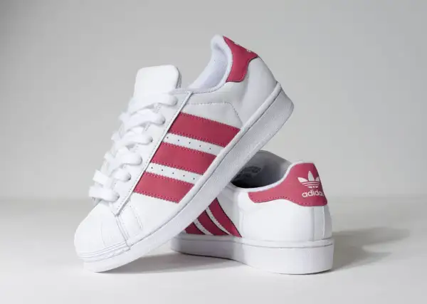 Białe buty Adidas Superstar z różowymi paskami i logo.