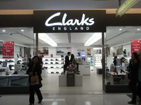 Sklep Clarks, znanej firmy obuwniczej z Anglii, oferuje szeroki wybór butów. Widać tu ekspozycję obuwia i klientów.