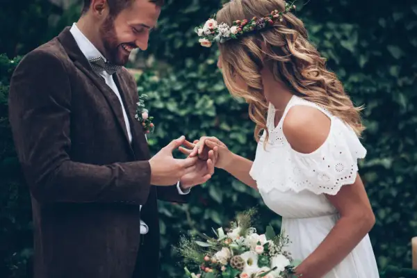 Para wesele w stylu boho: pan młody w brązowej marynarce i muszce, panna młoda w białej sukience i wianku.